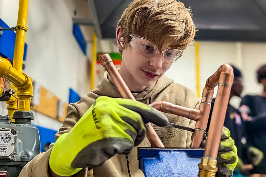 A Fusion Collegiate student soldering copper pipe fittings during hands-on plumbing training.